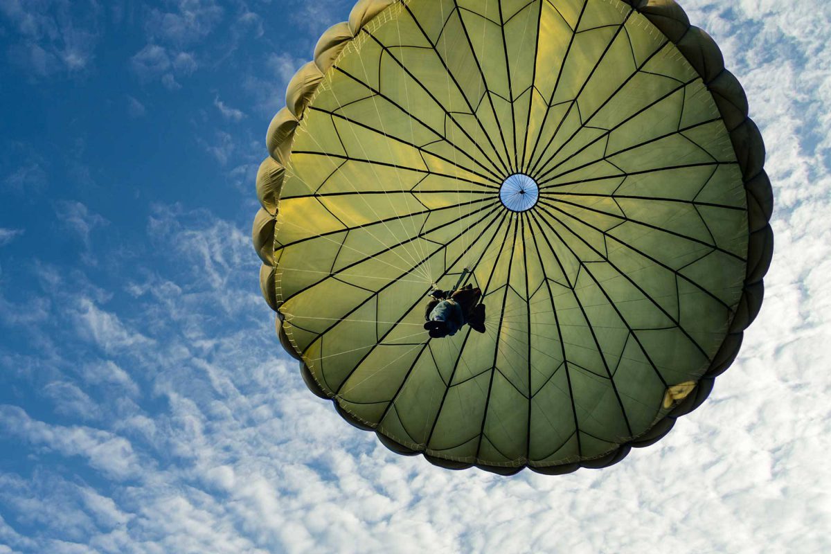 Skydiver nearing his landing with green canopy.